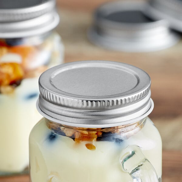 Two Arcoroc silver metal mini mason jars with yogurt and fruit inside, with a solid lid.