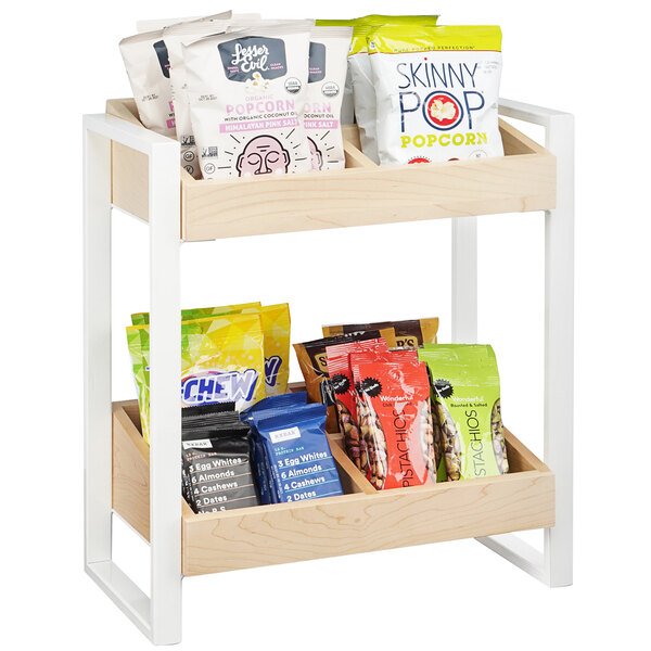A Cal-Mil two tier wooden organizer shelf with a variety of snacks including bags of popcorn.