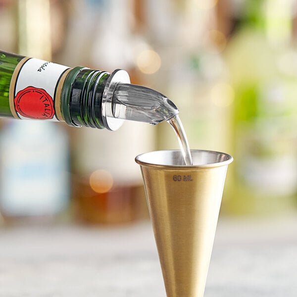 A person using a Choice Short Free Flow Smoke Liquor Pourer to pour a drink into a gold cup.