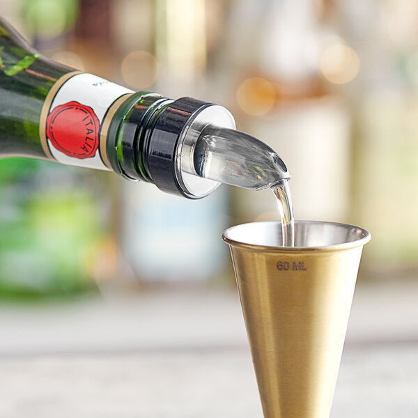 A bottle with a Choice Short Free Flow Smoke Liquor Pourer pouring liquid into a metal cup.