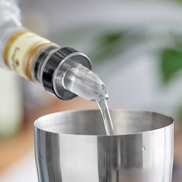 A person using a silver Choice Liquor Pourer to pour liquid into a metal cup.