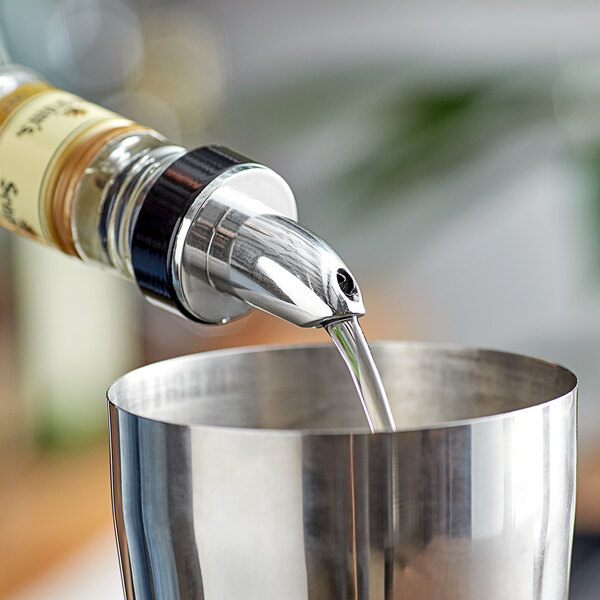 A person using a Choice Short Chrome Liquor Pourer to pour a drink from a bottle into a metal cup.
