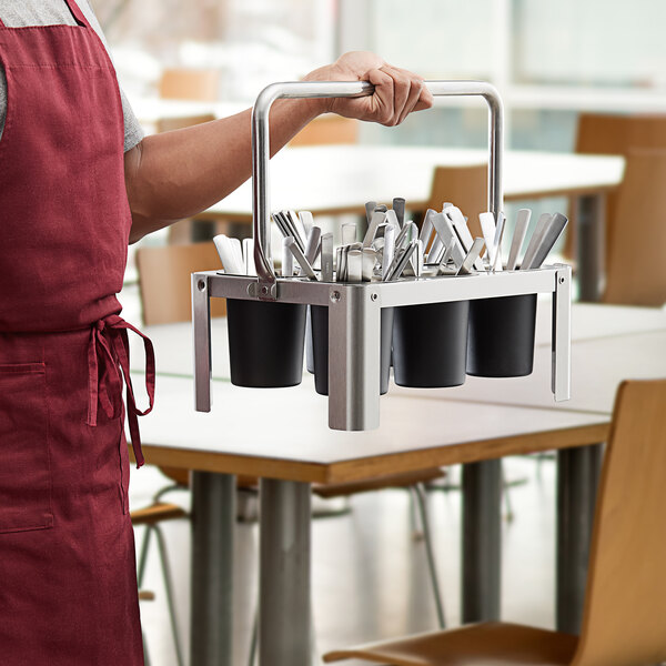 A person holding a stainless steel flatware carrier with utensils in it.