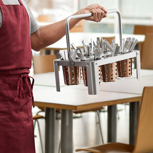A man holding a Choice stainless steel flatware carrier with copper perforated cylinders full of utensils.