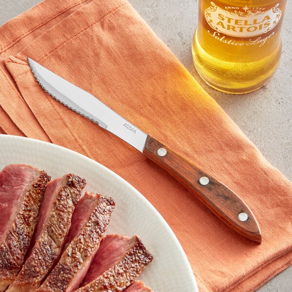 An Acopa steak knife next to a plate of meat.