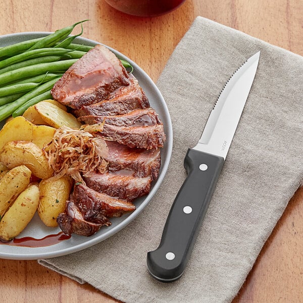 A plate of meat and vegetables on a napkin with an Acopa steak knife.