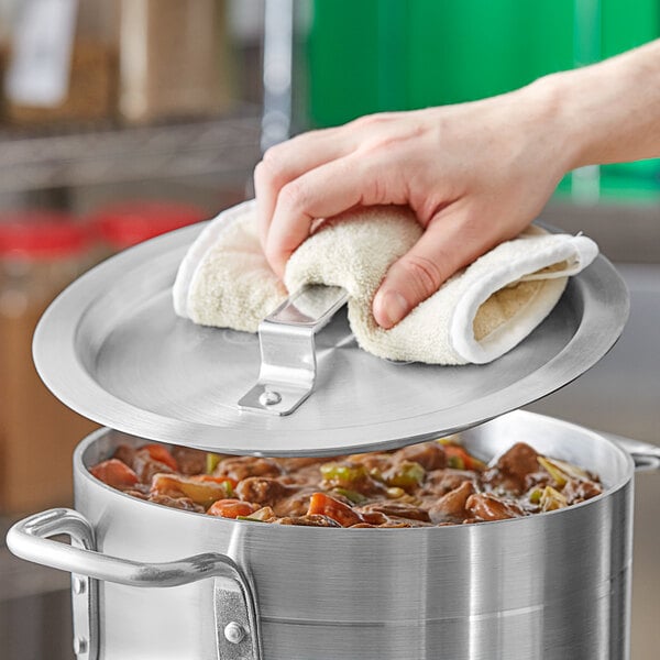 A hand holding a white towel over a Choice domed pot cover on a pot of food.