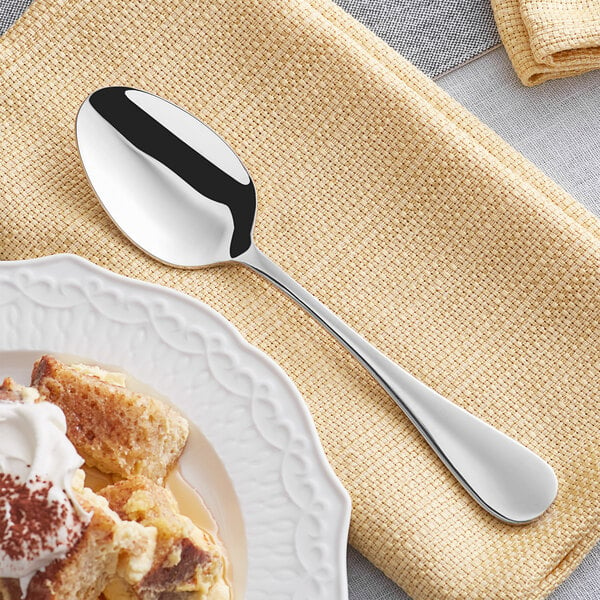 An Acopa Vittoria stainless steel oval bowl dessert spoon on a plate with cake.