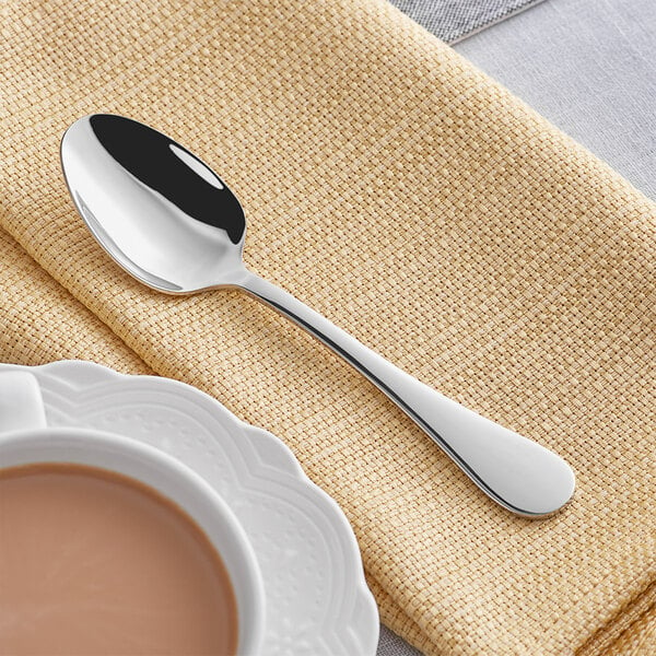 An Acopa Vittoria stainless steel teaspoon on a table next to a cup of tea.