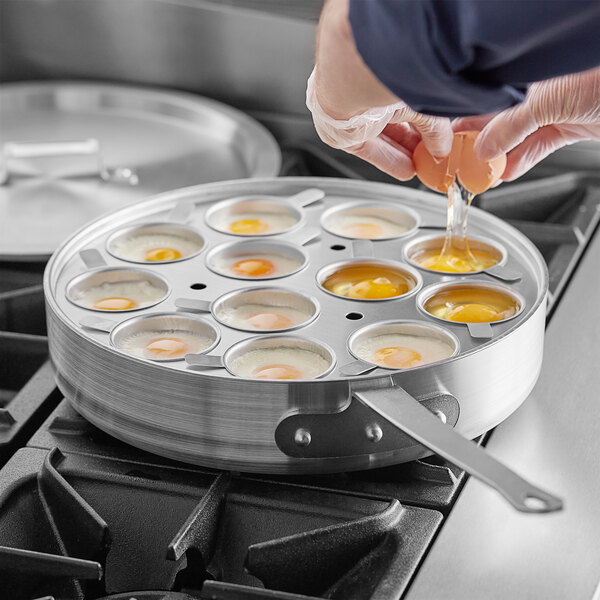 A person pouring an egg into a saute pan with metal cups inside.