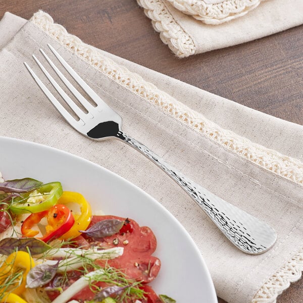 An Acopa Inspira stainless steel table fork on a plate of food on a table.