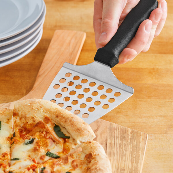 A person using an American Metalcraft perforated pizza server to slice a pizza.