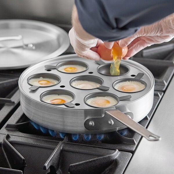 A person using the Choice 7-Cup Egg Poacher Set to fry eggs in a saute pan on a stove.
