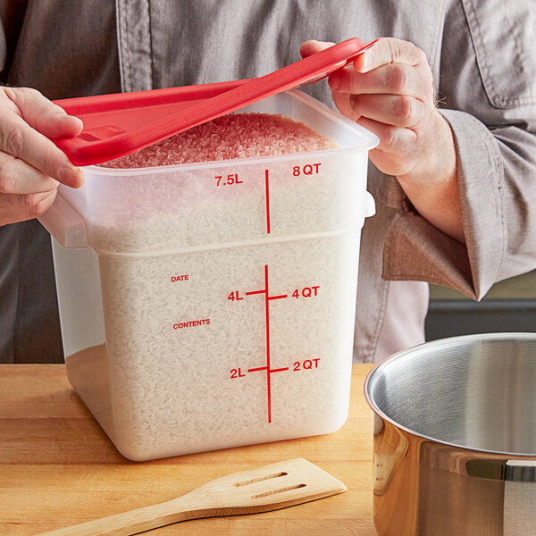 A person holding a Vigor translucent square food storage container filled with rice with a red lid.