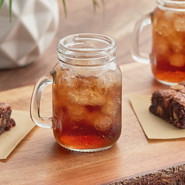 Two Arcoroc mini mason jars filled with brownies and ice on a table.