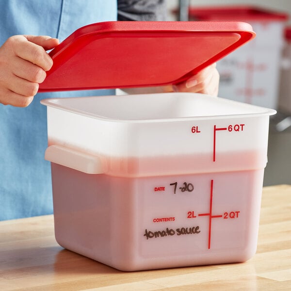 A woman's hand opening a red lid on a white square plastic food storage container.