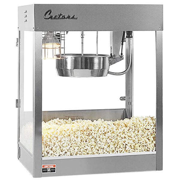 A Cretors popcorn machine with a silver and white finish popping popcorn.