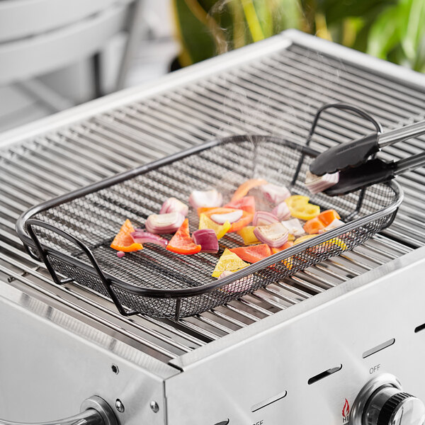 An Outset non-stick mesh grill basket filled with vegetables on a grill.