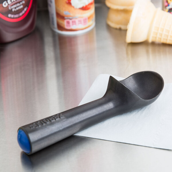 A Zeroll Zerolon ice cream scoop on a counter next to a cup of ice cream.