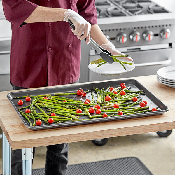 A person using tongs to serve asparagus from a Baker's Mark sheet pan.