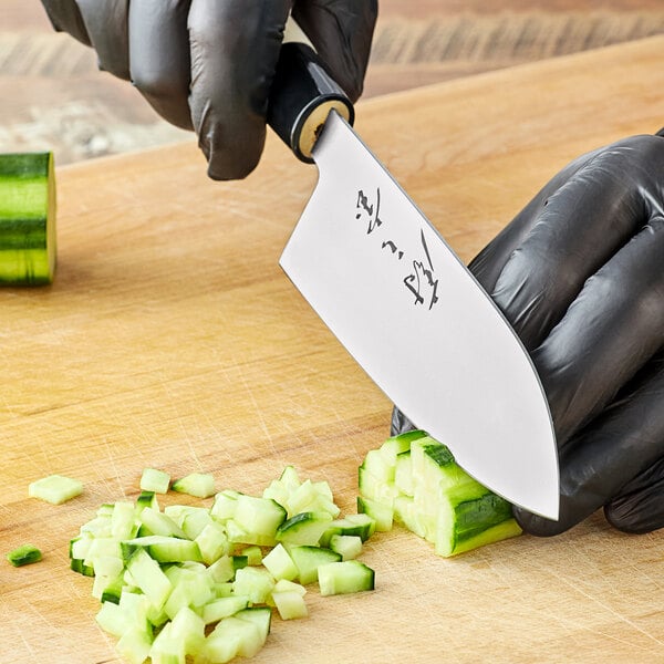 A person in black gloves uses a Mercer Culinary Santoku knife to cut cucumbers on a counter in a professional kitchen.
