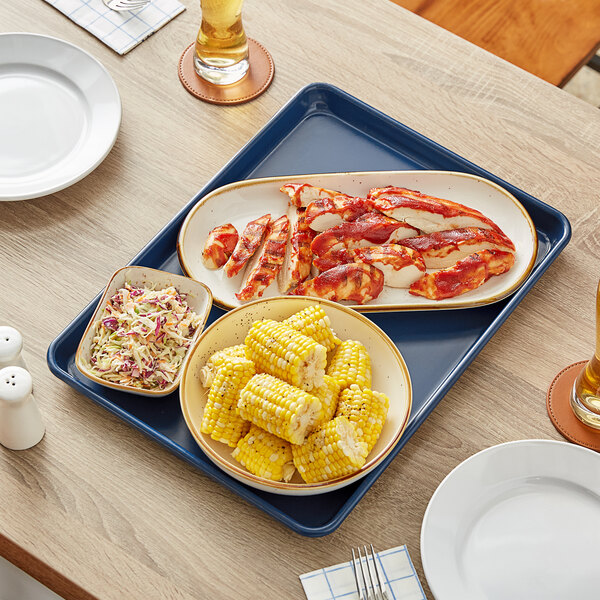 A Baker's Mark dark blue non-stick aluminum sheet pan with corn on the cob, coleslaw, and other food on it.