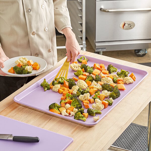 A person using a spatula to stir vegetables on a Baker's Mark non-stick sheet pan.