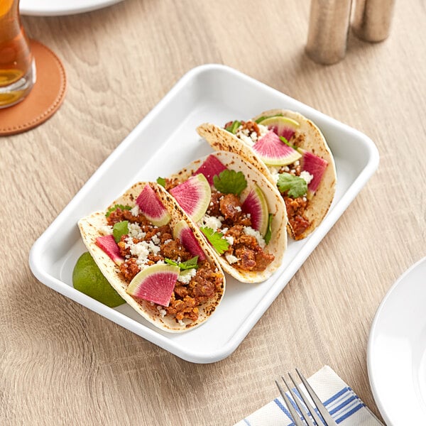A Baker's Mark white metal tray with two tacos, watermelon radish, and cheese on it.