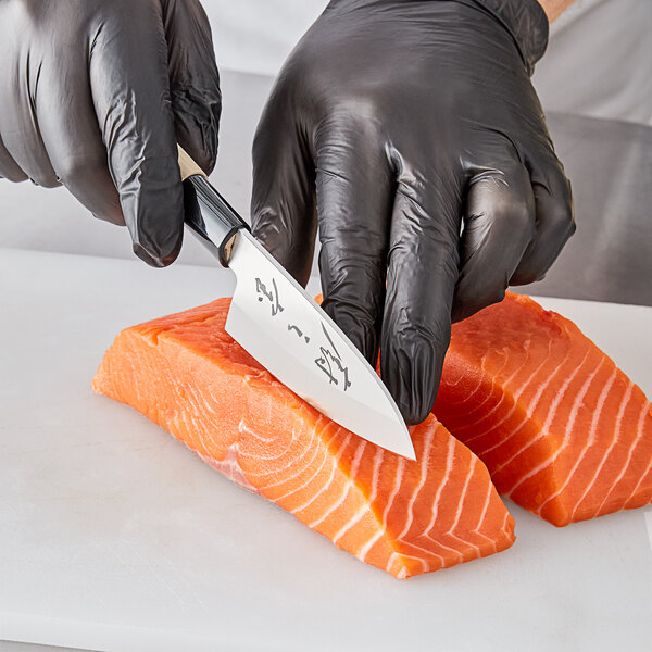 A person in black gloves using a Mercer Culinary Deba knife to cut a piece of salmon.