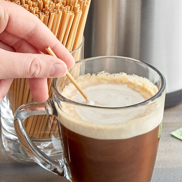 A person stirring a cup of coffee with a HAY! wheat straw.