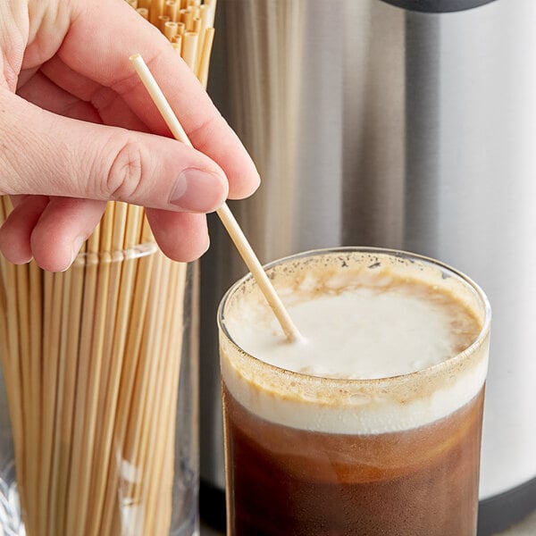 A person holding a HAY! wheat straw in a glass of coffee.