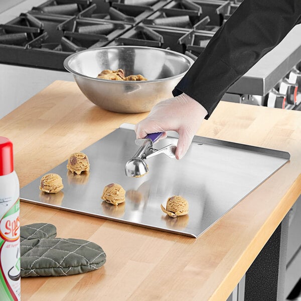 A person using a spatula to put cookies on a Baker's Mark rimless aluminum cookie sheet.