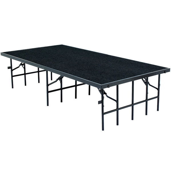 A National Public Seating portable stage with black carpet on a rectangular table.