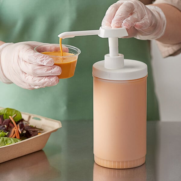 A person wearing gloves using a Choice condiment pump to pour orange liquid into a plastic container.