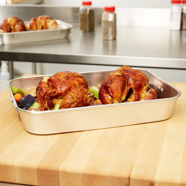 A Vollrath aluminum roasting pan filled with cooked chicken and vegetables on a table.