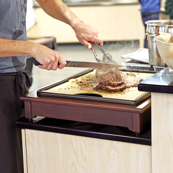 A person using a Cal-Mil Westport Carving Station to cut meat on a cutting board.