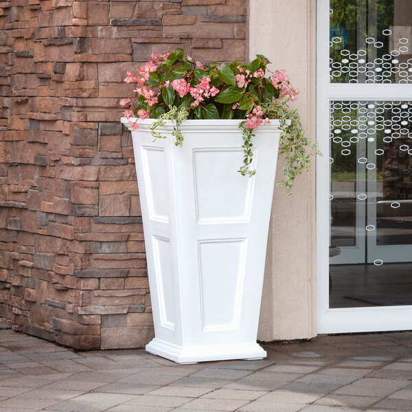 A white Mayne Fairfield planter with pink flowers in it.