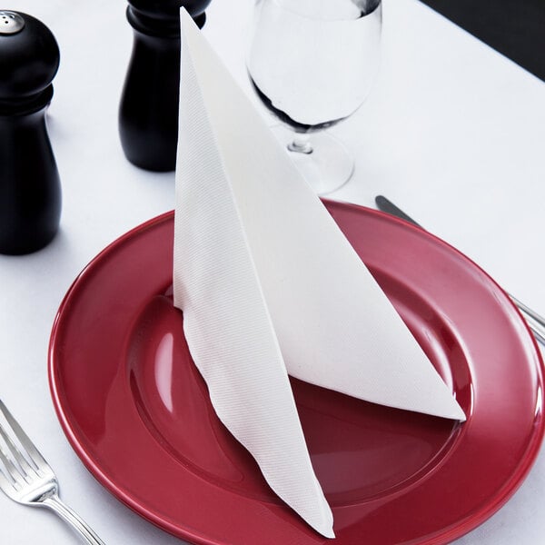 A white Hoffmaster FashnPoint linen-feel napkin folded on a red plate with silverware.
