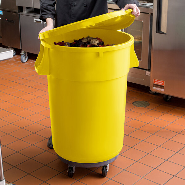 A man in a chef's uniform using a yellow mobile ingredient storage bin in a school kitchen.