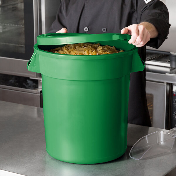 A chef holding a green 10 gallon ingredient storage bin full of pasta.