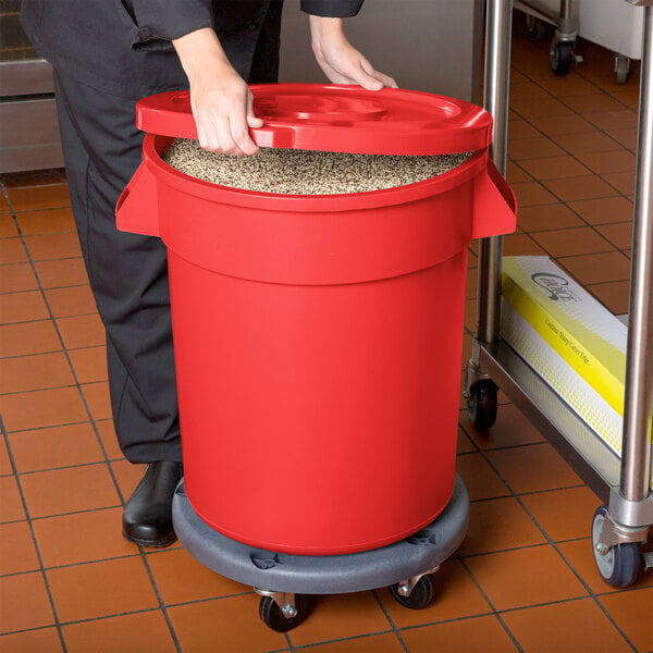 A woman using a red mobile ingredient storage bin to hold rice in a school kitchen.
