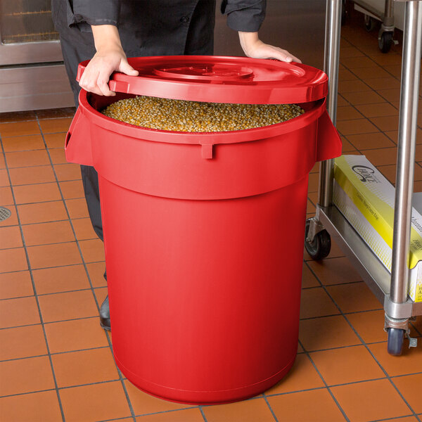 A woman holding a red round ingredient storage bin full of corn.