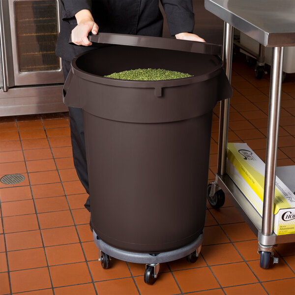 A woman in a school kitchen holding a brown mobile ingredient storage bin full of green beans.