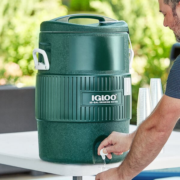 A man pouring water into a green Igloo Turf Series insulated beverage dispenser on a table.