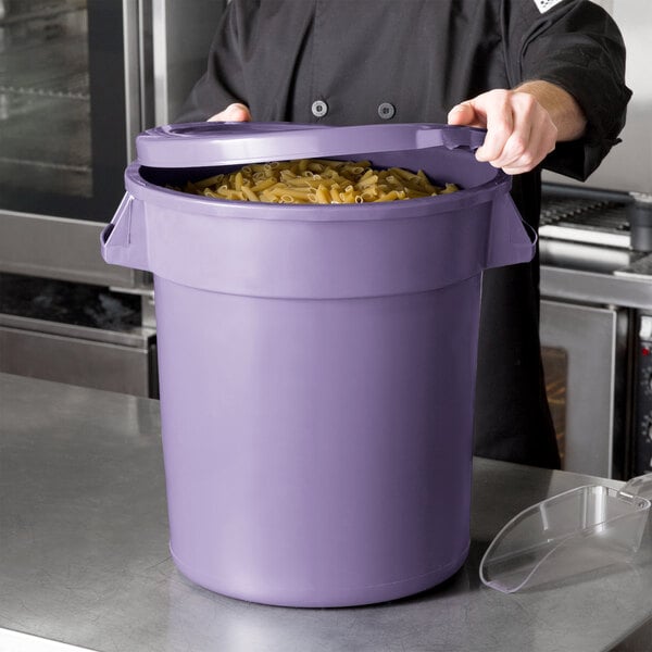 A person holding a purple round ingredient storage bin full of pasta.