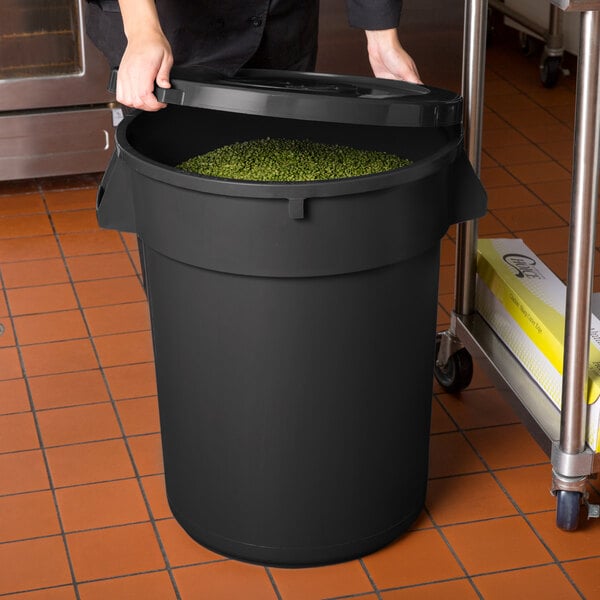 A woman holding a black round ingredient storage bin with green food inside.