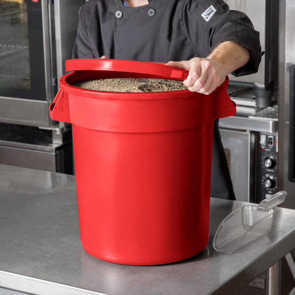 A man in a chef's uniform holding a red round ingredient storage bin with a lid full of food.