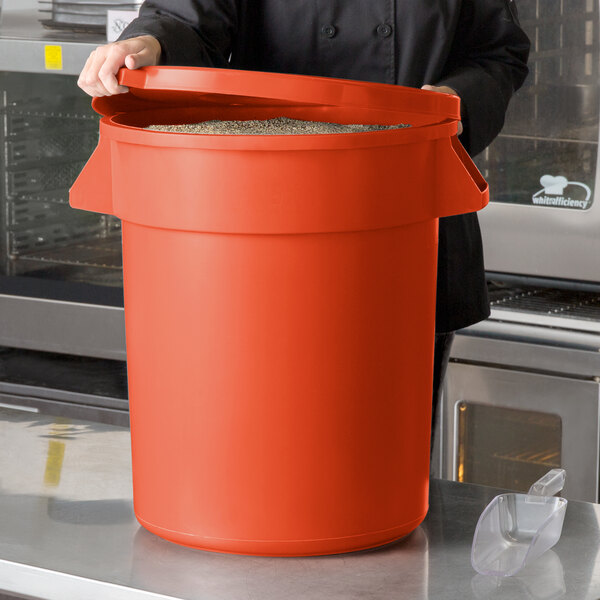 A woman in a chef's uniform holding a large orange round ingredient storage bin with a lid.