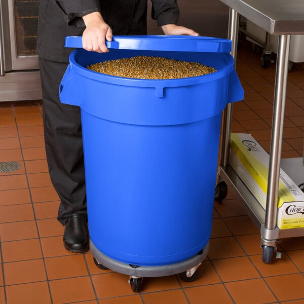 A man in a chef's uniform holding a blue mobile ingredient storage bin full of food.
