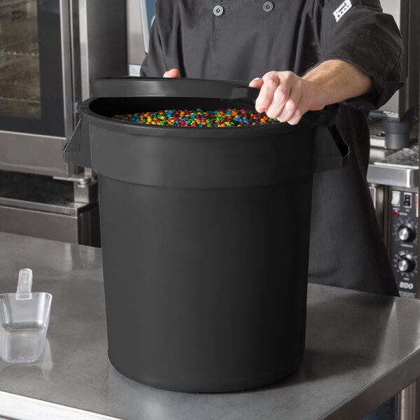 A person holding a 10 gallon black ingredient storage bin full of colorful candies.